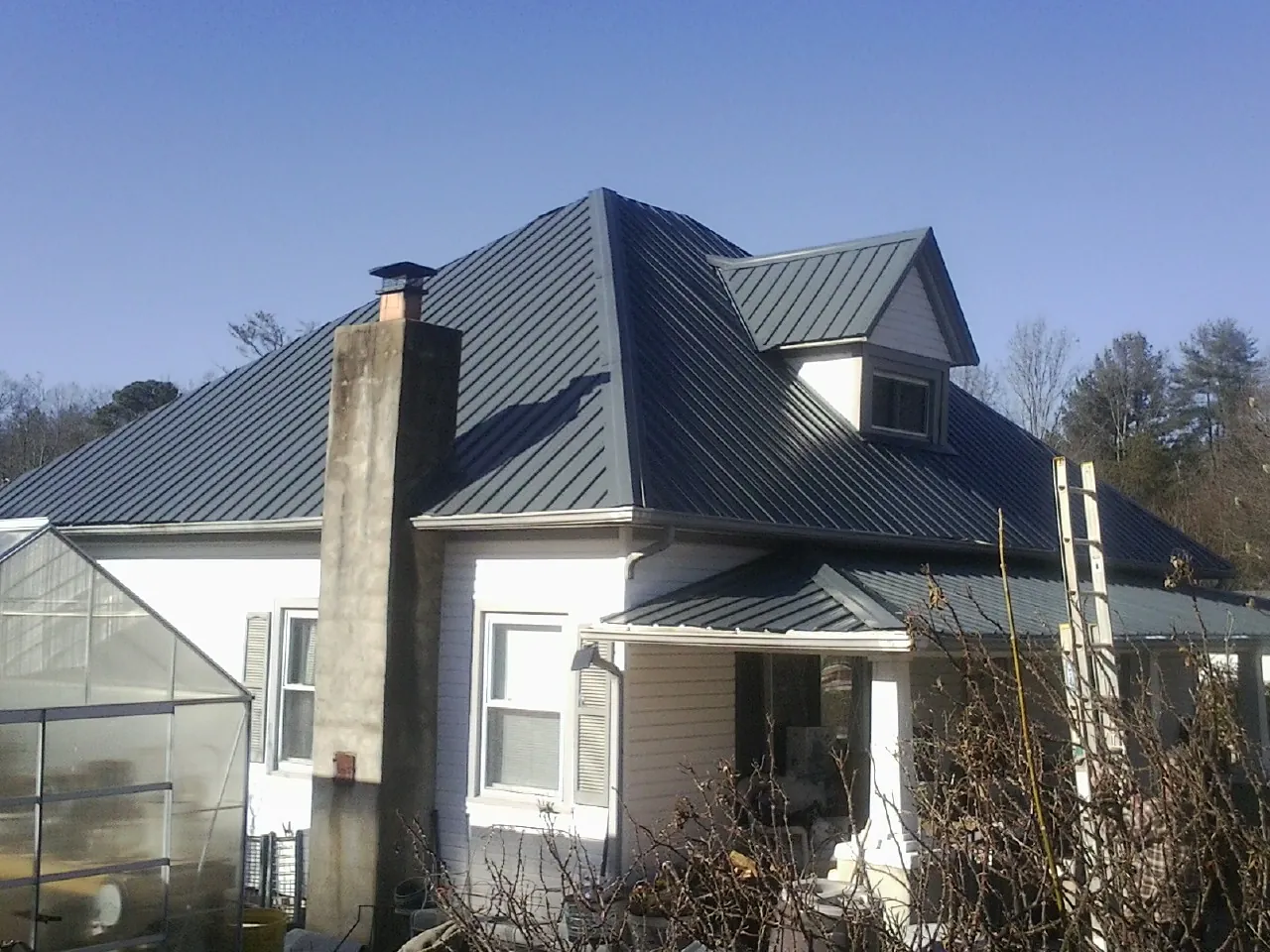 Dark blue standing seam metal roof on a white farmhouse with dormer — Slate & Tile Roof Repair by Roofing Brothers in West Babylon