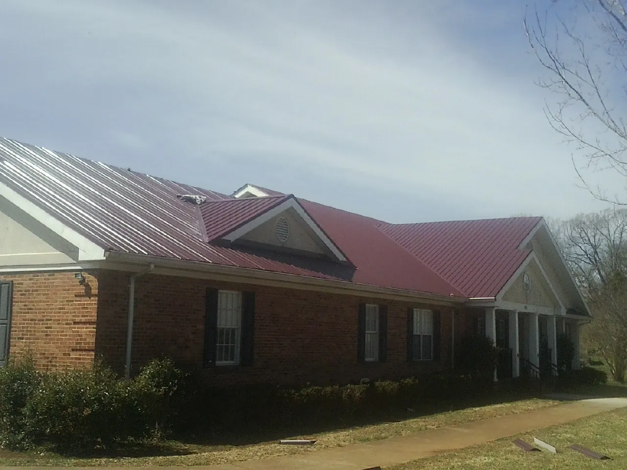 Red metal roof with gabled entries on a long brick building, from a Hail Damage Roof Repair job in West Babylon