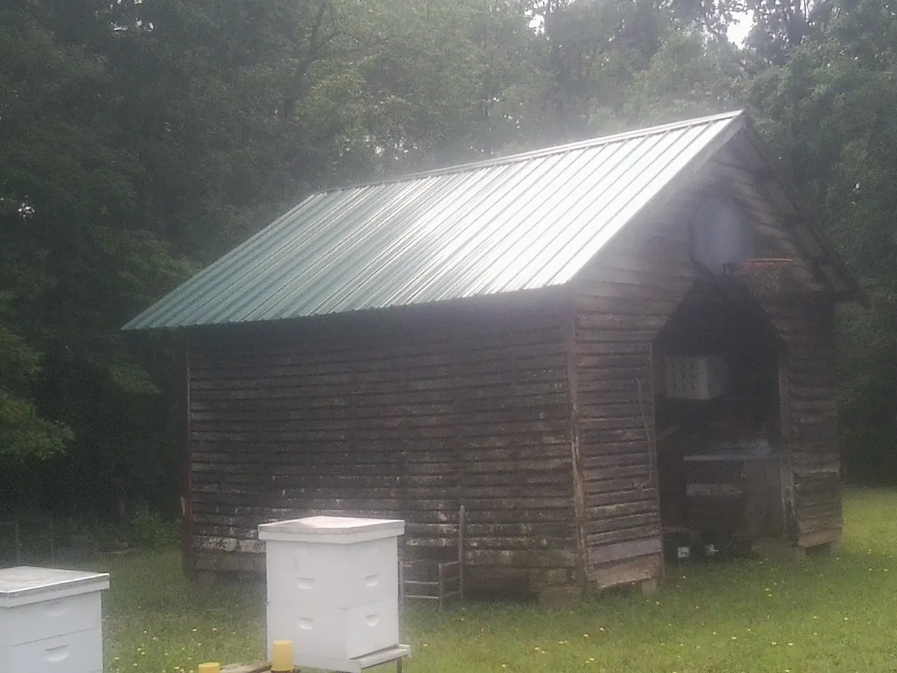 Green metal roof on a weathered barn beside stacked beehives in West Babylon