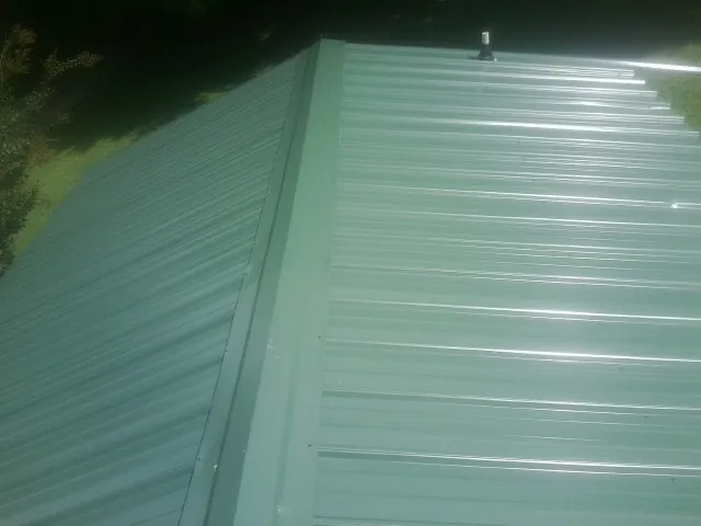 New green metal panels meeting at the ridge of a roof — Flat Roof Repair work by our crew in West Babylon