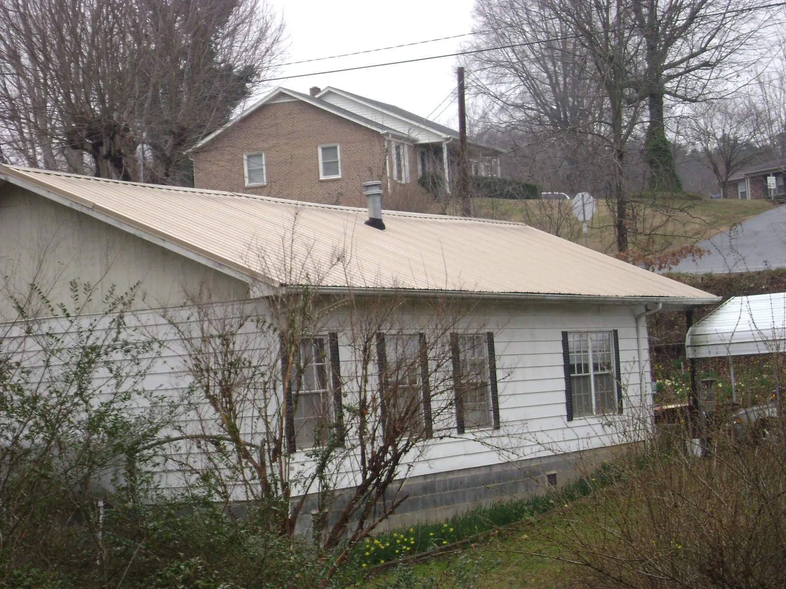 Tan metal roof on a white sided house set into a hillside — Commercial Roofing by Roofing Brothers in West Babylon